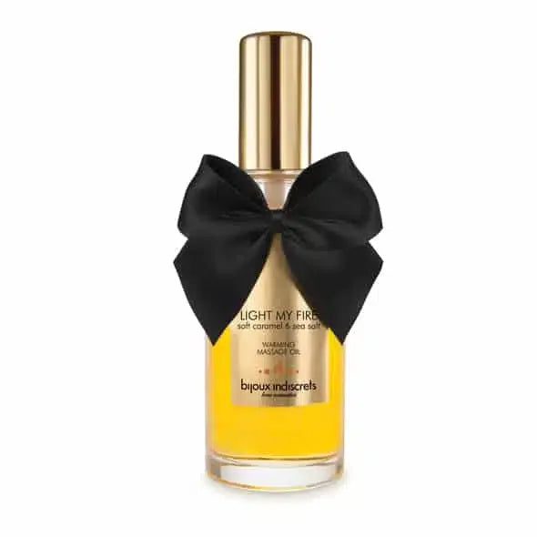 Warming massage oil bottle with gold cap and black bow, labeled Light My Fire, caramel scent