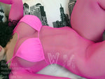 Realistic love doll in pink fishnet bodysuit and lingerie on a sofa with cityscape pillow.