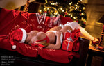 Lifelike female doll in festive lingerie with Santa hat, lying on a sofa near Christmas tree with wrapped gifts.