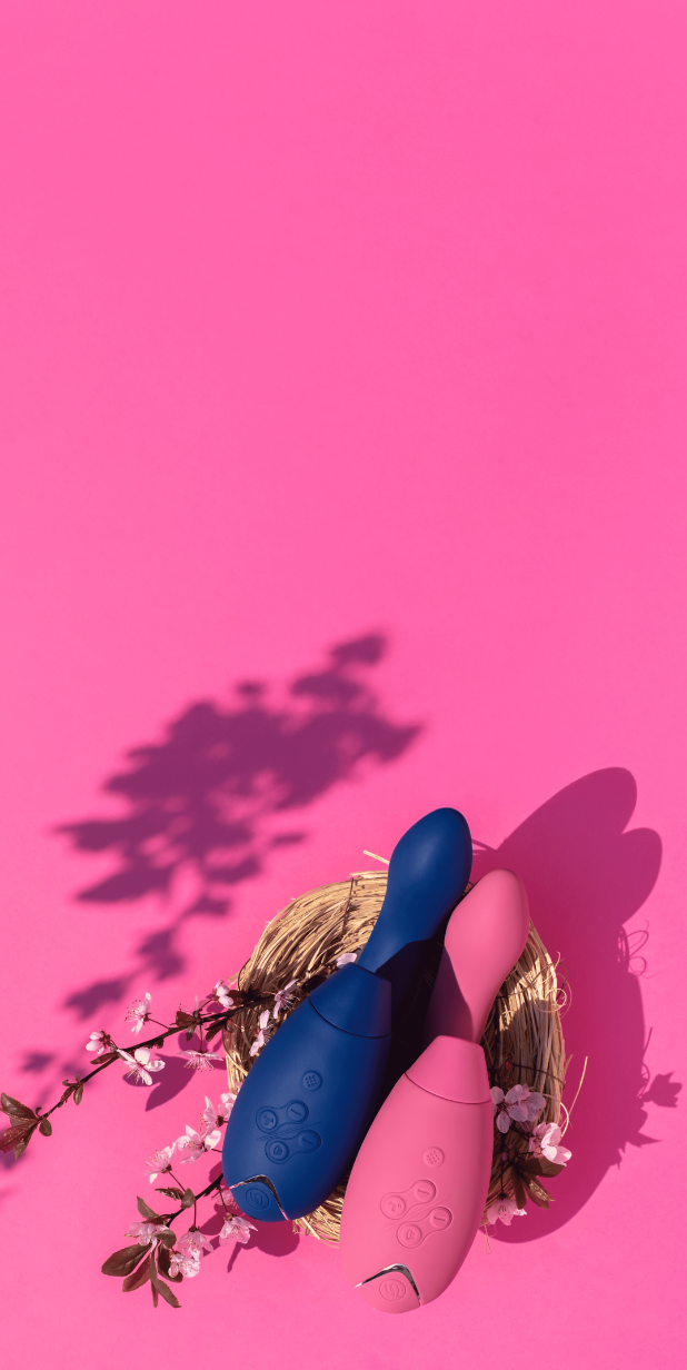 Erotiske sexleketøy i rosa og blå farger plassert i en påskekurv med blomster på rosa bakgrunn