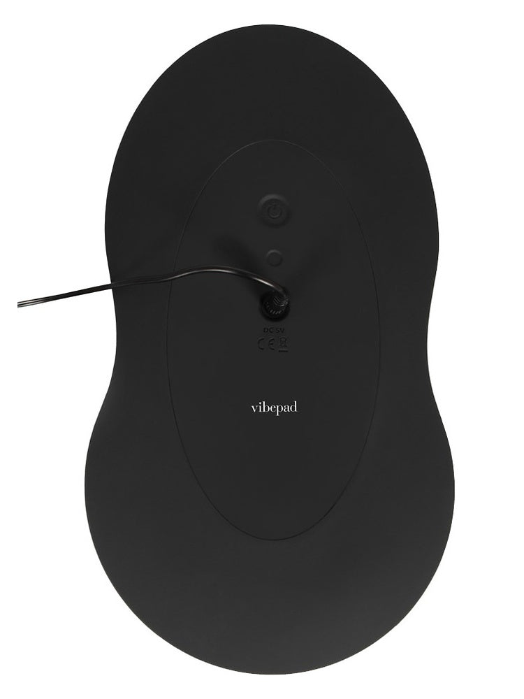 Undersiden av Vibepad 3 med av/på-knapp, ladeport, logo og tilkoblet USB-ladekabel.